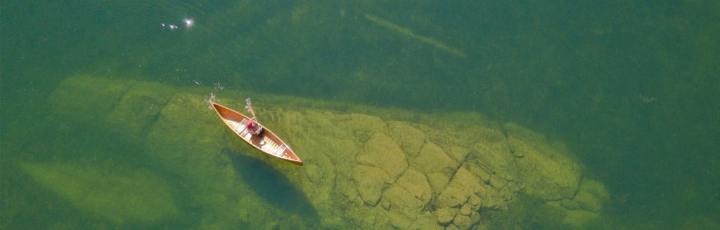 Red canoe crossing clear green lake water