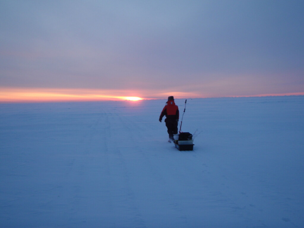 Ice fisher on a frozen lake at sunset