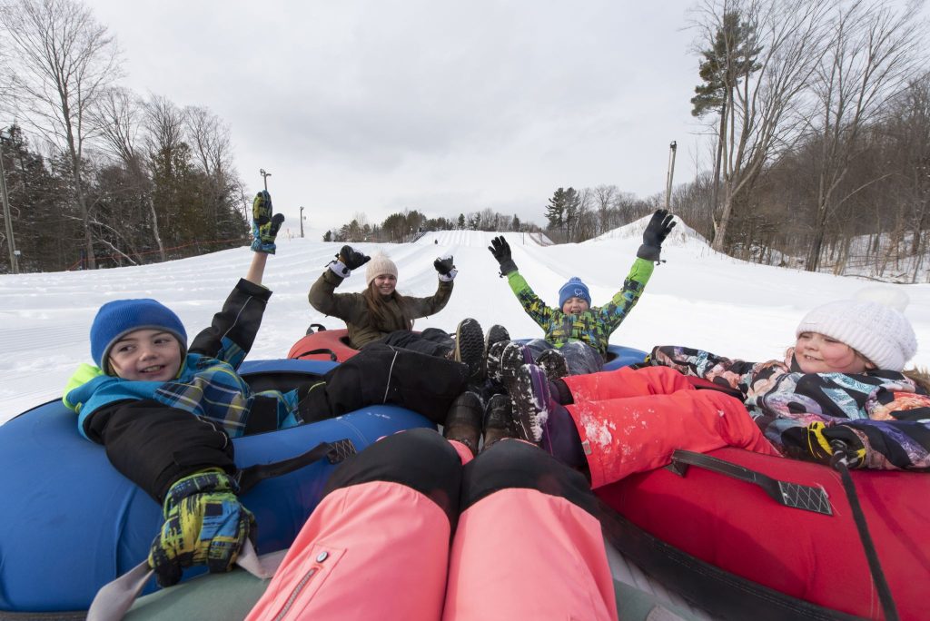 Children and adults snow tubing down a hill