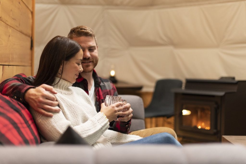 Glen Oro Farm couple cuddling on a couch holding warm drinks by a wood fire stove