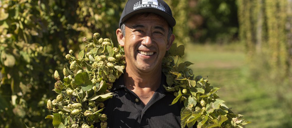 Smiling farm owner standing among hop vines